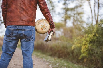 Canvas Print - Male wearing a leather jacket and jeans holding a desk globe and the bible with blurred background