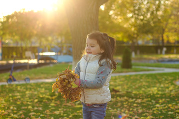 a smiling child holds in his hands an armful of yellow fallen leaves.