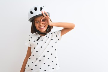 Poster - Beautiful child girl wearing security bike helmet standing over isolated white background doing ok gesture with hand smiling, eye looking through fingers with happy face.