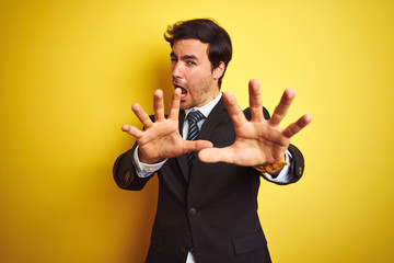 Sticker - Young handsome businessman wearing suit and tie standing over isolated yellow background afraid and terrified with fear expression stop gesture with hands, shouting in shock. Panic concept.