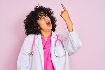 Sticker - Young arab doctor woman with curly hair wearing stethoscope over isolated pink background pointing finger up with successful idea. Exited and happy. Number one.