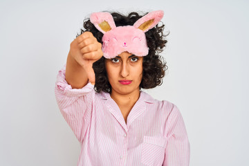 Sticker - Arab woman with curly hair wearing pajama and sleep mask over isolated white background looking unhappy and angry showing rejection and negative with thumbs down gesture. Bad expression.