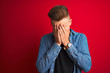 © Krakenimages.com - Young handsome man wearing denim shirt standing over isolated red background with sad expression covering face with hands while crying. Depression concept.