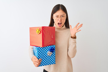 Canvas Print - Young chinese woman holding birthday gifts over isolated white background crazy and mad shouting and yelling with aggressive expression and arms raised. Frustration concept.