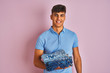 © Krakenimages.com - Young indian shopkeeper man holding folded jeans standing over isolated pink background with a happy face standing and smiling with a confident smile showing teeth
