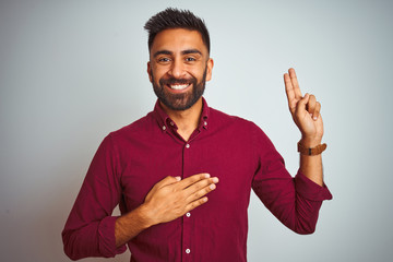 Young indian man wearing red elegant shirt standing over isolated grey background smiling swearing with hand on chest and fingers up, making a loyalty promise oath