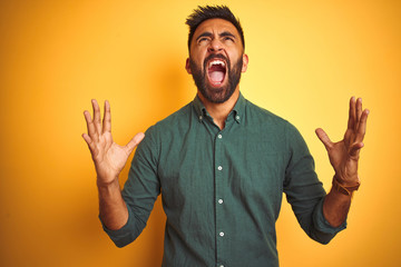 Wall Mural - Young indian businessman wearing elegant shirt standing over isolated white background crazy and mad shouting and yelling with aggressive expression and arms raised. Frustration concept.