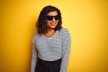 Wall Mural - Transsexual transgender woman wearing sunglasses over isolated yellow background looking away to side with smile on face, natural expression. Laughing confident.