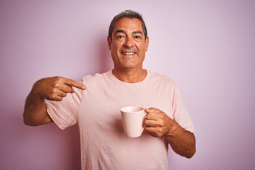 Wall Mural - Handsome middle age man holding cup of coffee standing over isolated pink background very happy pointing with hand and finger