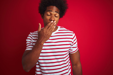 Poster - Young african american man with afro hair wearing striped t-shirt over isolated red background bored yawning tired covering mouth with hand. Restless and sleepiness.