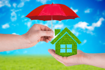 Hand hold red umbrella protect green grass house on blue sky background