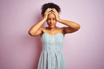 Poster - African american woman wearing casual striped dress standing over isolated pink background suffering from headache desperate and stressed because pain and migraine. Hands on head.