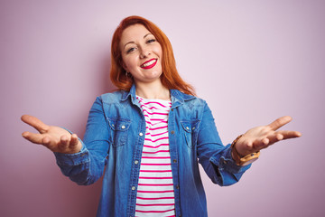 Poster - Beautiful redhead woman wearing denim shirt and striped t-shirt over isolated pink background smiling cheerful offering hands giving assistance and acceptance.