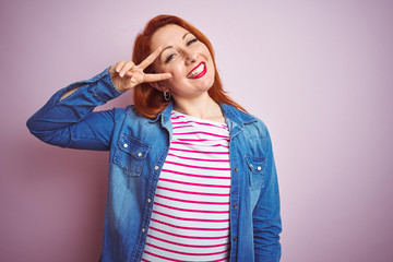 Poster - Beautiful redhead woman wearing denim shirt and striped t-shirt over isolated pink background Doing peace symbol with fingers over face, smiling cheerful showing victory