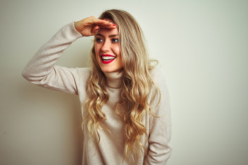 Sticker - Beautiful woman wearing winter turtleneck sweater over isolated white background very happy and smiling looking far away with hand over head. Searching concept.