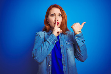 Canvas Print - Young beautiful redhead woman wearing denim shirt standing over blue isolated background asking to be quiet with finger on lips pointing with hand to the side. Silence and secret concept.