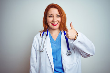 Wall Mural - Young redhead doctor woman using stethoscope over white isolated background doing happy thumbs up gesture with hand. Approving expression looking at the camera showing success.