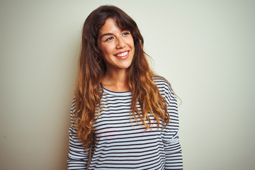 Wall Mural - Young beautiful woman wearing stripes t-shirt over white isolated background looking away to side with smile on face, natural expression. Laughing confident.