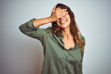 Wall Mural - Young beautiful woman wearing green shirt standing over grey isolated background smiling and laughing with hand on face covering eyes for surprise. Blind concept.