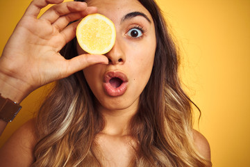 Canvas Print - Young beautiful woman holding a lemon on eye over yellow isolated background scared in shock with a surprise face, afraid and excited with fear expression