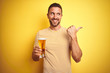 © Krakenimages.com - Young handsome man drinking a pint glass of beer over isolated yellow background pointing and showing with thumb up to the side with happy face smiling
