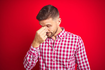 Poster - Young handsome man over red isolated background tired rubbing nose and eyes feeling fatigue and headache. Stress and frustration concept.