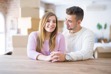 Wall Mural - Young beautiful couple sitting on the table at home, hugging in love very happy for moving to new home with cardboard boxes behind them