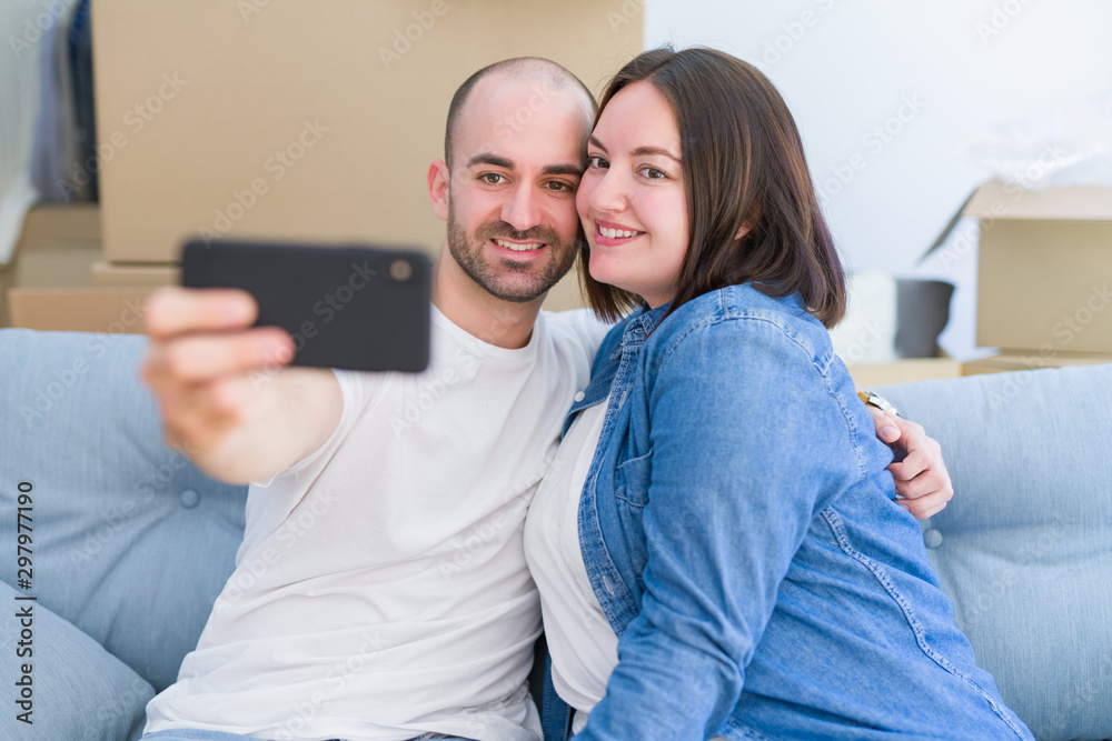 Young couple sitting on the sofa at new home taking a selfie photo ...