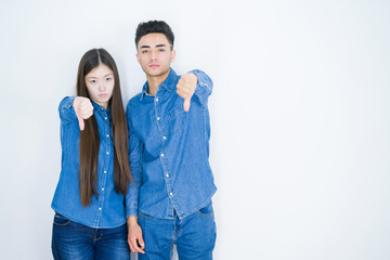 Sticker - Beautiful young asian couple over white isolated background looking unhappy and angry showing rejection and negative with thumbs down gesture. Bad expression.