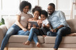 © fizkes - Happy parents with kids relax on sofa with tablet