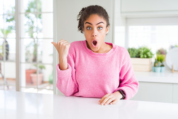 Sticker - Beautiful african american woman with afro hair wearing casual pink sweater Surprised pointing with hand finger to the side, open mouth amazed expression.