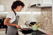 © nenadaksic - Mixed race woman in apron standing next to stove and stirring tomato sauce. On stove are saucepan and pot with spaghetti.