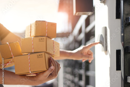 Fotomural Delivery man holding parcel boxes and ring the doorbell on the client's door in the morning background