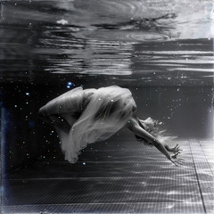 Wall Mural - Black and white image. Underwater photo beautiful blonde wearing in white flying dress, swimming in pool underwater.