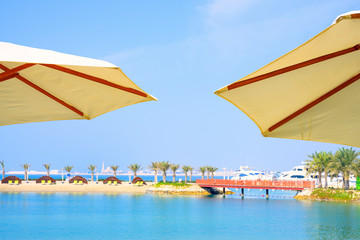 Wall Mural - Two umbrella in front of bridge across island with sea water over blue sky background.