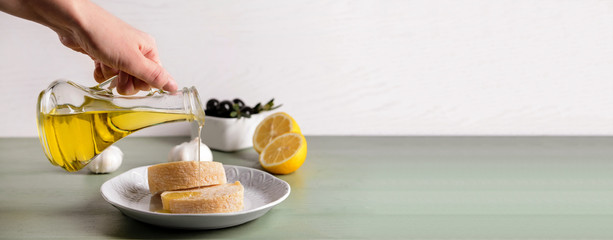 Wall Mural - Woman pouring tasty olive oil from bottle onto fresh bread