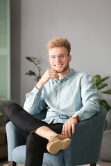 Sticker - Portrait of stylish young man sitting in armchair at home