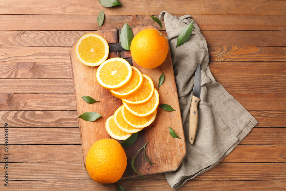 Board with sliced oranges and knife on wooden table