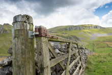 Close-up, Shallow Focus Of An Damaged And Abandoned Fence Seen Broken To One Side. A Rock Wall Is Extending To The Distance In The Picturesque Yorkshire Dales.