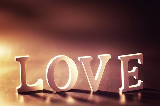 Wooden and metal letters forming word LOVE written on dark black background with lights.