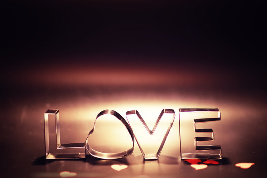 Wooden and metal letters forming word LOVE written on dark black background with lights.