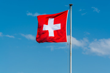 National flag of Switzerland flying at the Zurich lake against blue sky