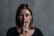 © Ermolaev Alexandr - Young beaten up woman looking at camera and holding finger on mouth. Empty space for text