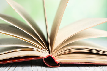 Wall Mural - Open book on white wooden table against blurred green background, closeup