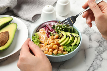 Woman eating delicious avocado salad with chickpea at white marble table, closeup