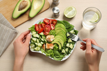 Woman eating delicious avocado salad with fried chicken at wooden table, top view