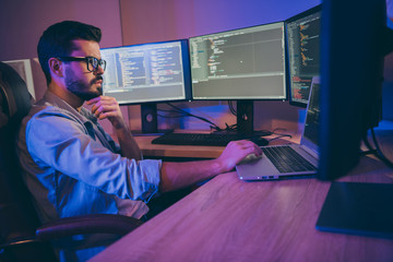 Profile photo of it specialist guy sitting comfy office chair holding hand on keyboard looking many monitors checking website debugging expert dark office indoors