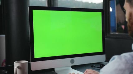 Modern computer greenscreen mock-up monitor close-up. Side view young business man working on personal computer keyboarding in corporate office space.