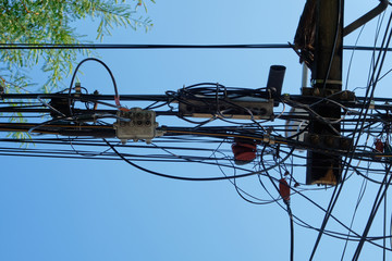 Tangled and messy of electric wires on electric pole in the city with sky background.