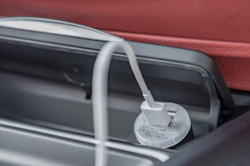 Wall Mural - Close-up, isolated view of a automotive cigarette lighter being used as a USB phone charger. The background shows some of the red leather of this german car.